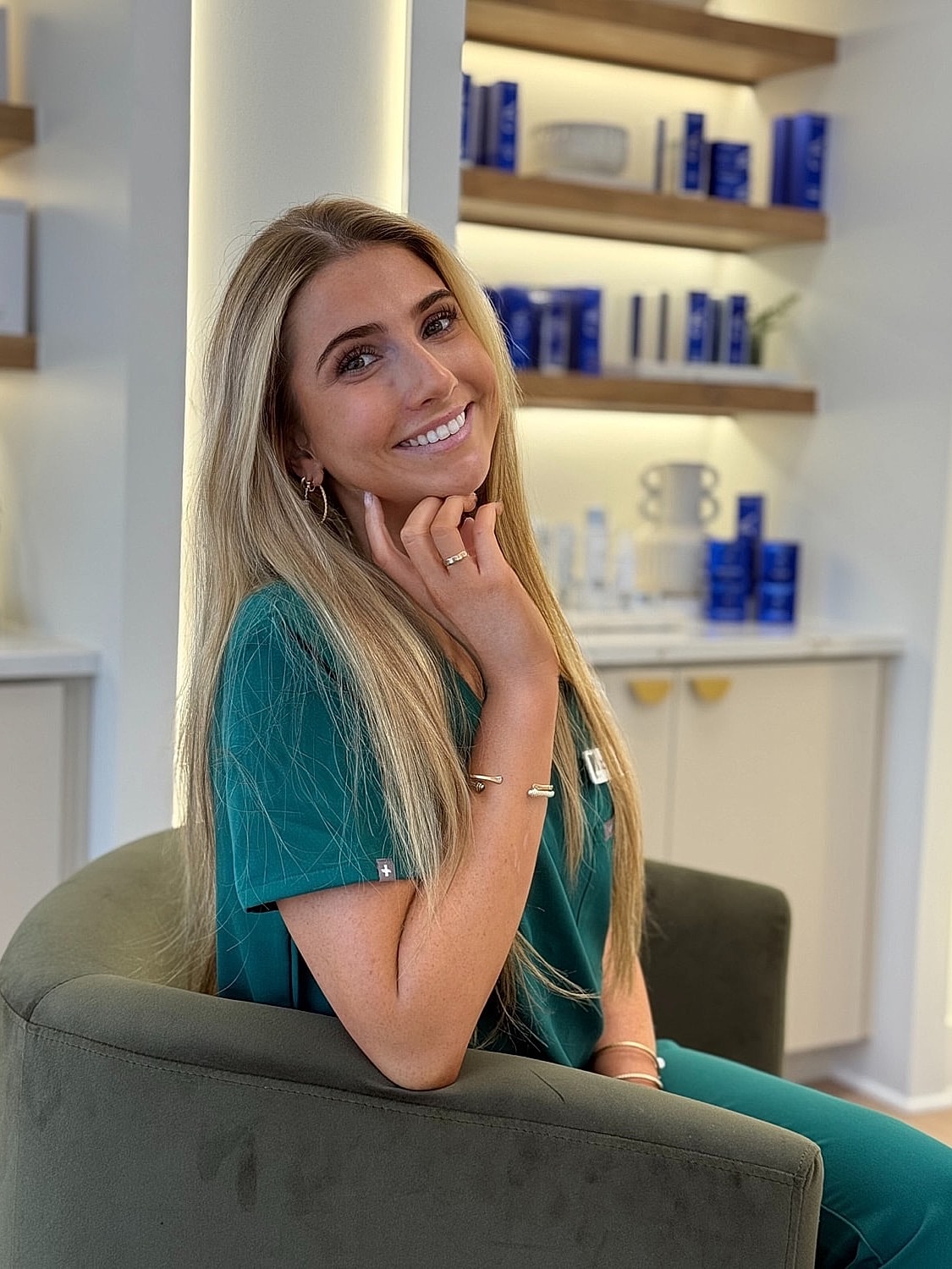 Smiling woman in green scrubs sitting comfortably.