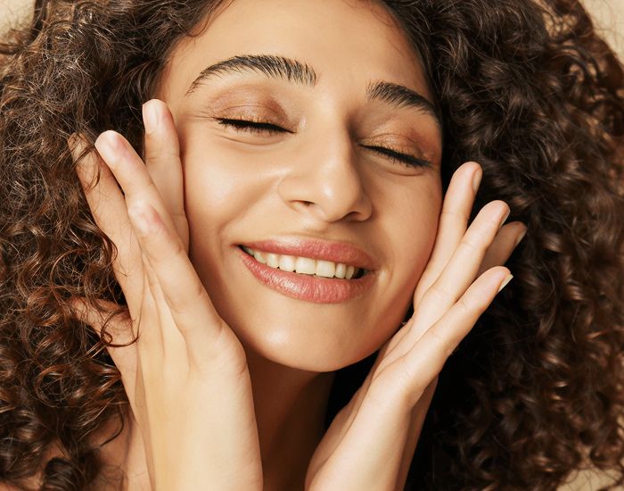Smiling woman with curly hair and glowing skin.