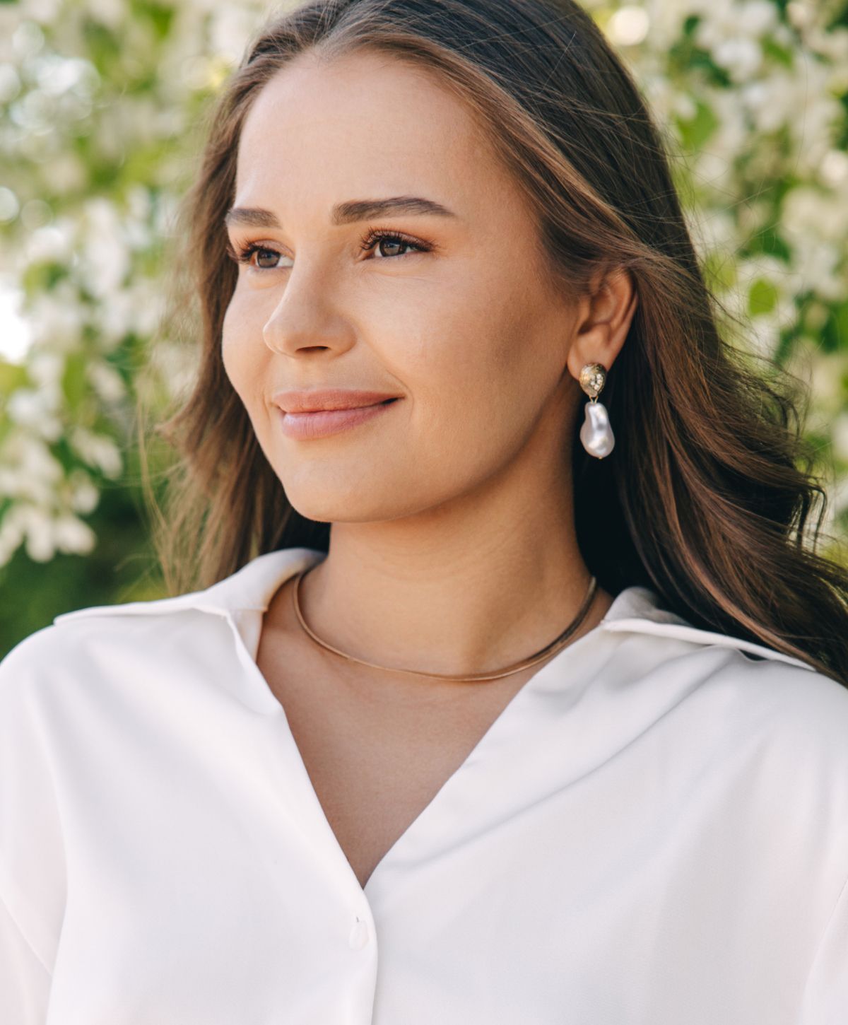 Woman with earrings and a white blouse outdoors.