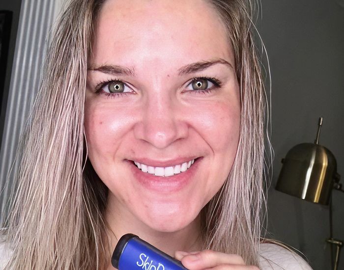 Smiling woman holding skincare product, bright background.