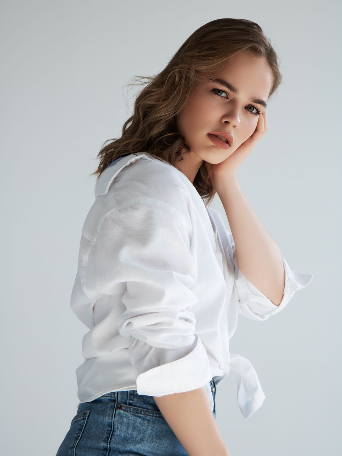 Woman in white shirt posing thoughtfully against backdrop.