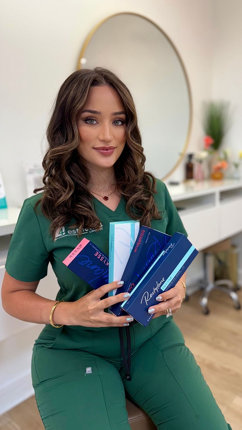 Woman in scrubs holding skincare product boxes.