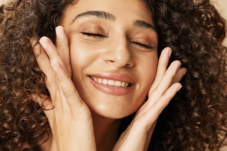 Smiling woman with curly hair, hands on face.